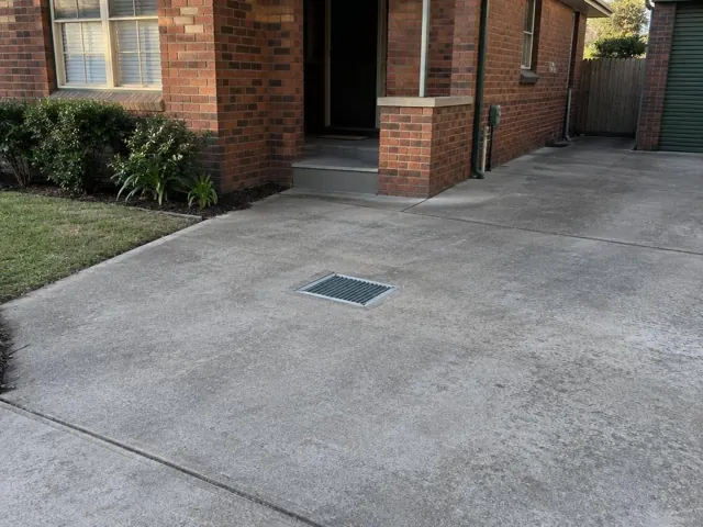 Concrete driveway with a small metal gully grate beside a brick house in Mayfield