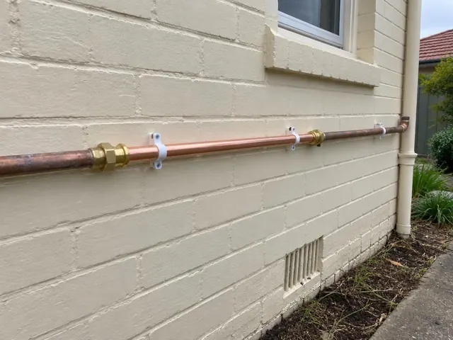 Repaired copper water pipe on painted brick exterior wall in Broadmeadow