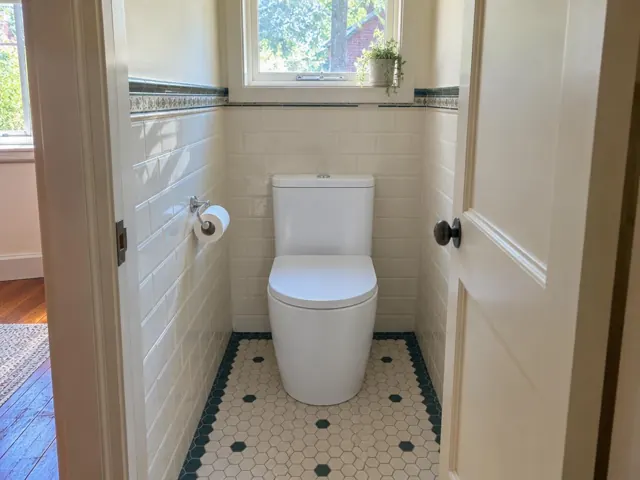 White toilet in a small tiled bathroom with a window and patterned floor in Georgetown